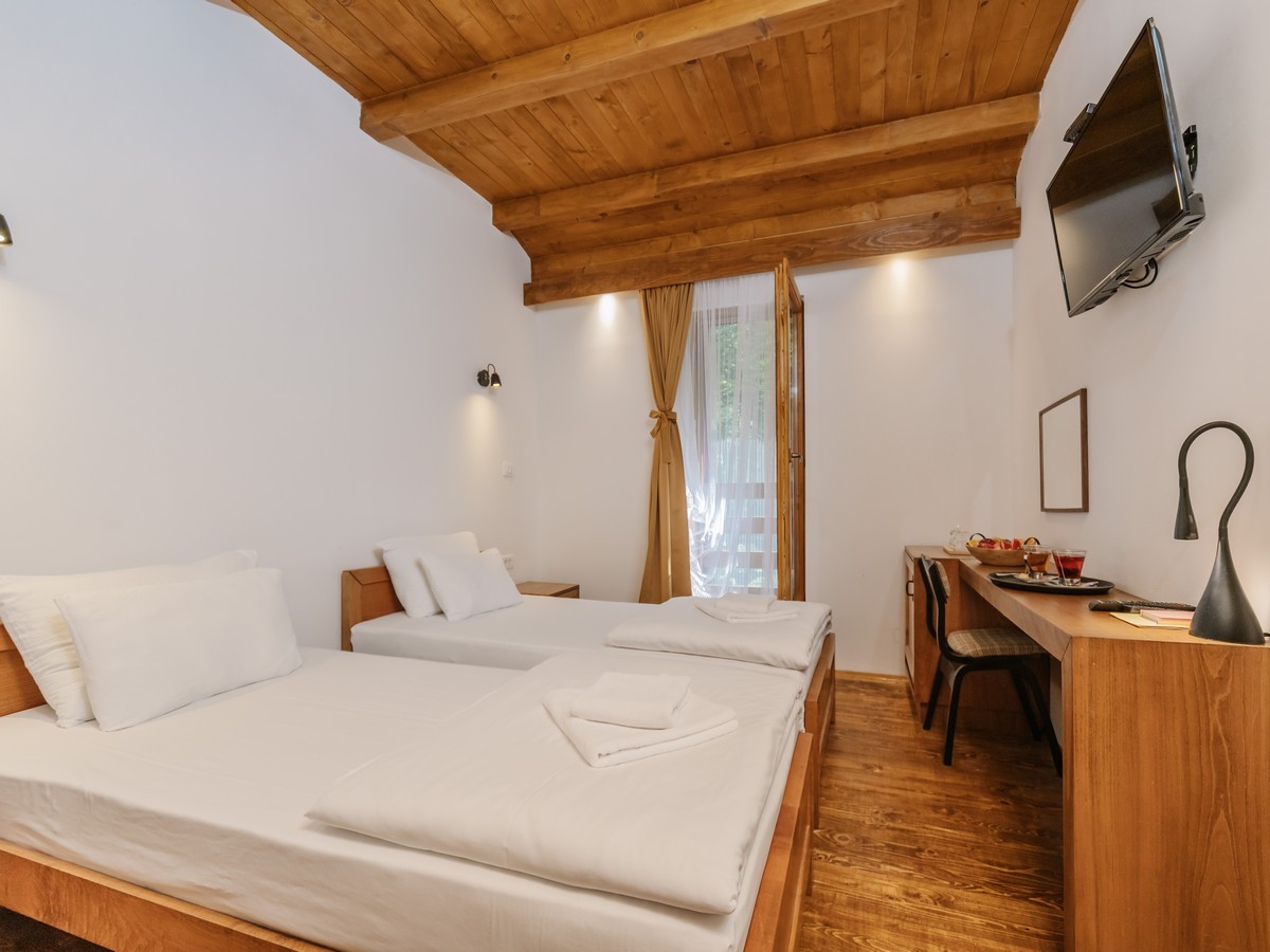 Moderna hotelska soba sa drvenim stropom, dva kreveta i radnim stolom pored prozora