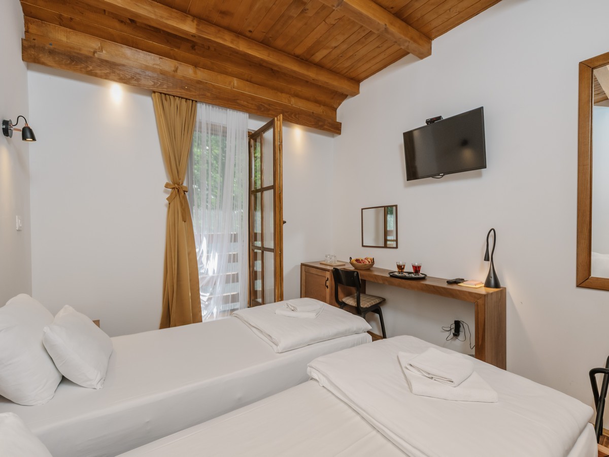 Hotelska soba sa dva kreveta, drvenim gredama na plafonu i pogledom na terasu