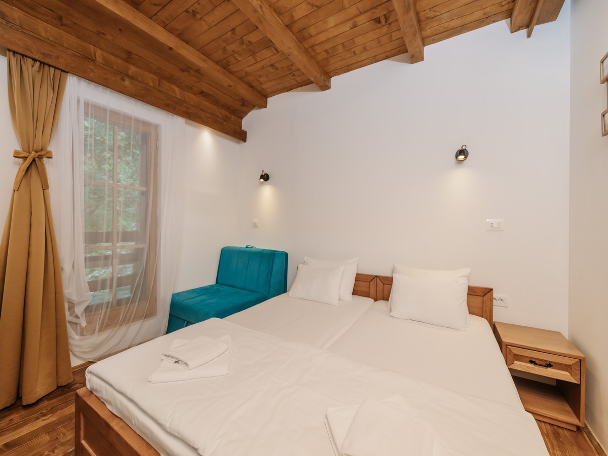 Moderna hotelska soba sa drvenim gredama, bijelim zidovima, krevetom sa belim posteljinama i tirkiznom sofom