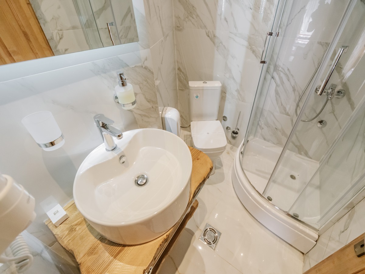 Moderan hotelski kupatilo sa mramornim pločicama, okruglim umivaorom i tuš kabinom